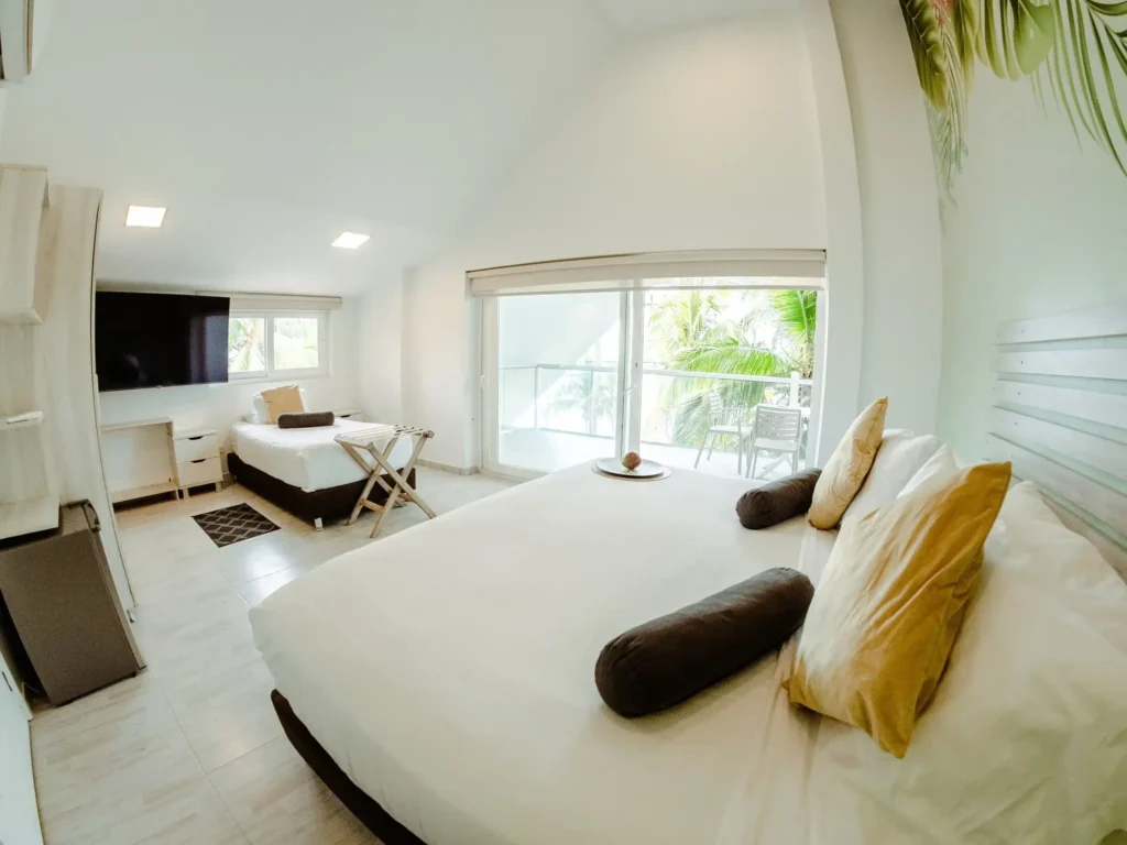 habitacion estandar triple cuenta con una cama doble y una individual cuenta con una decoracion de tonos neutros ventanales amplios que ofrece una vista directa al balcon